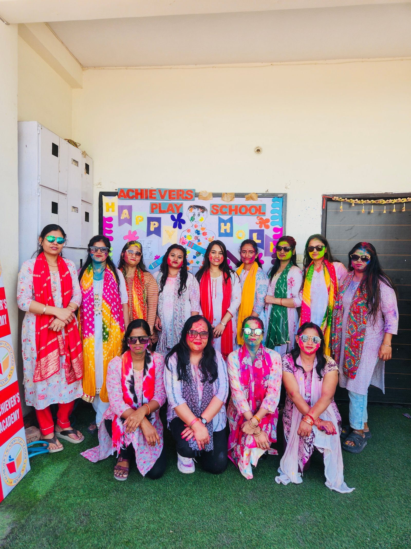 Holi Celebration - School teachers and staff with color on faces in front of Holi banner